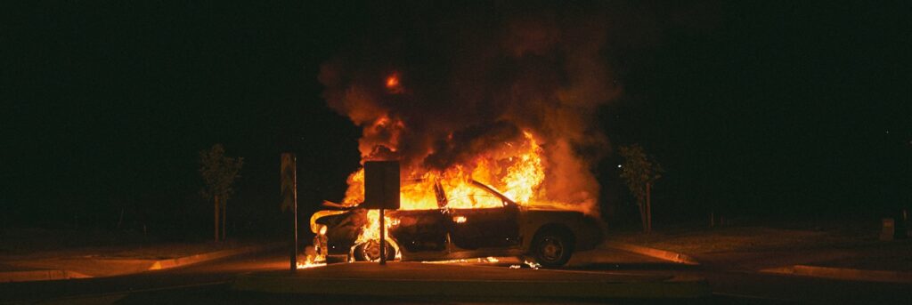 burning grey sedan near trees and signboard at night